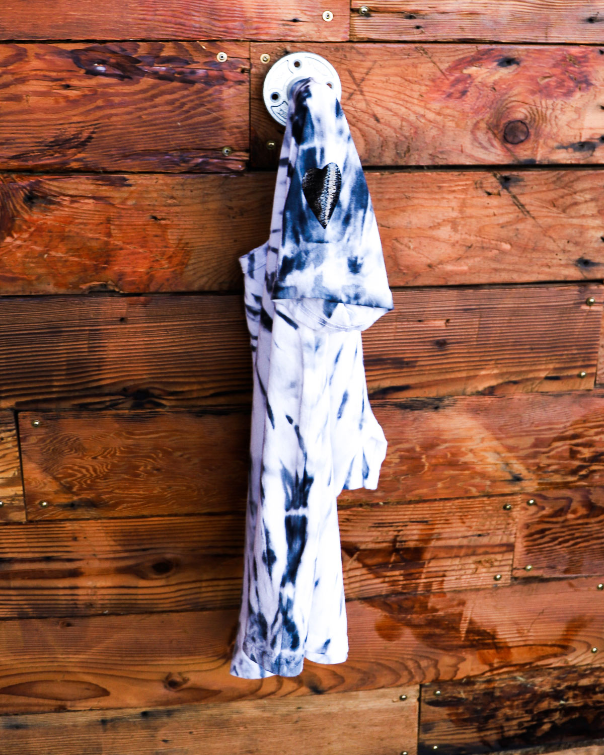 White hand dyed spiral tie dye t-shirt on a hanger in front of a weathered wood wall