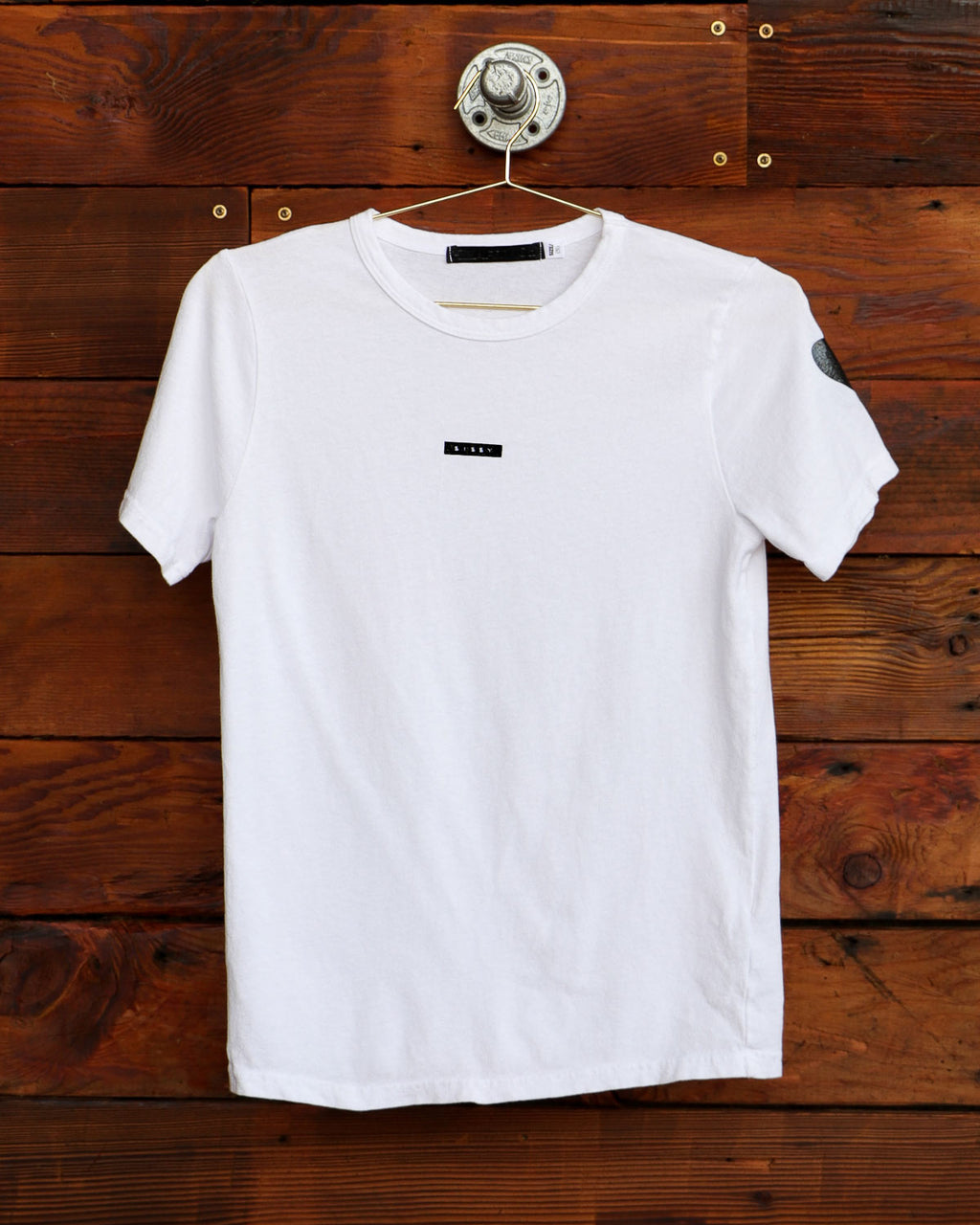 White Sissy label t-shirt hanging on weathered wood wall