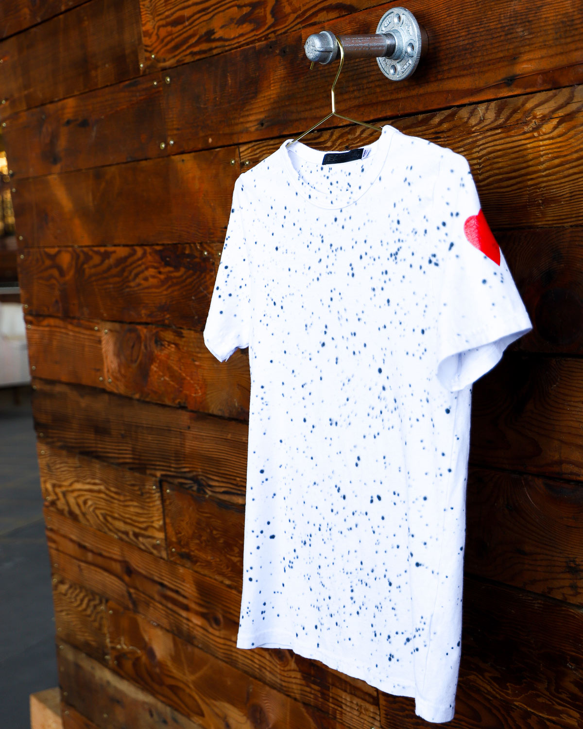 White splatter hand dyed tie dye t-shirt hanging on wood wall