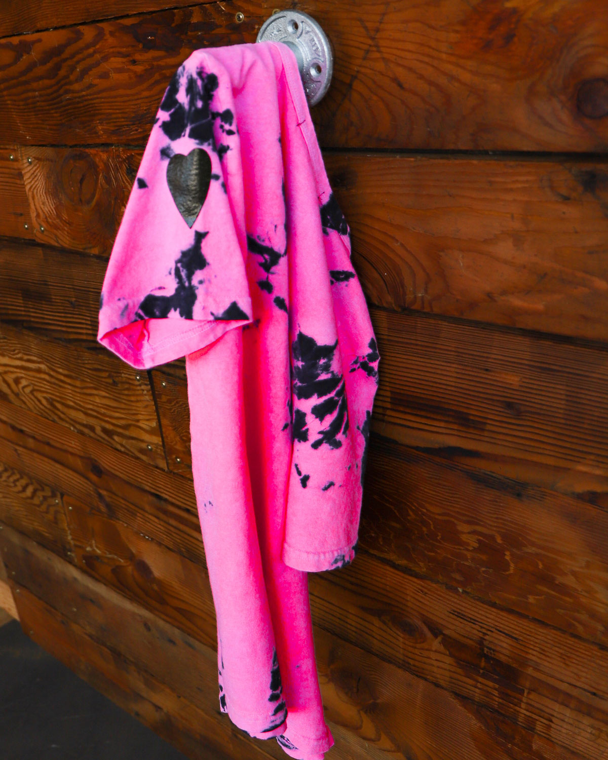 Pink and black hand dyed tie dye shirt hanging on wood wall