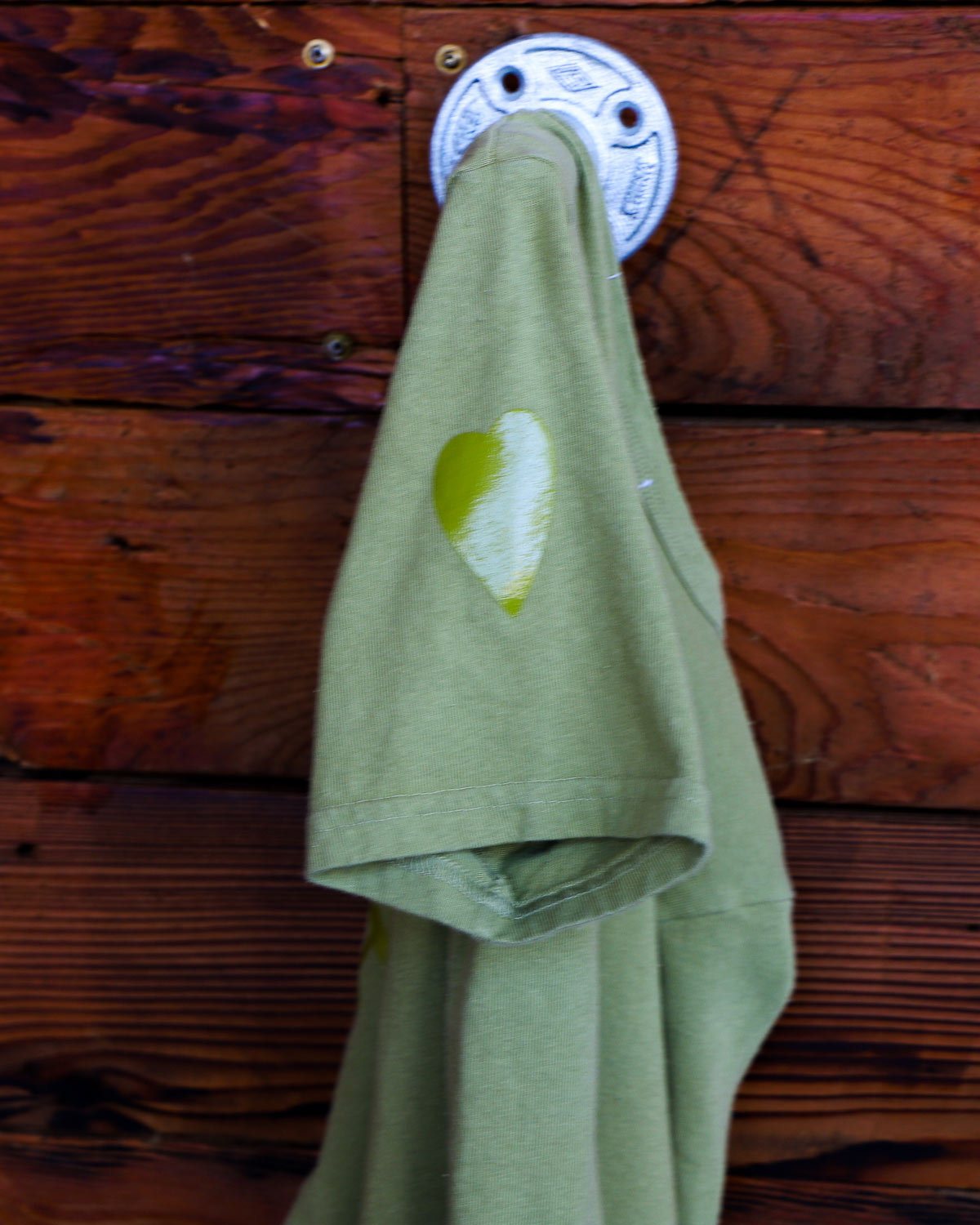 Green stealth Heart On logo t-shirt hanging on wood wall