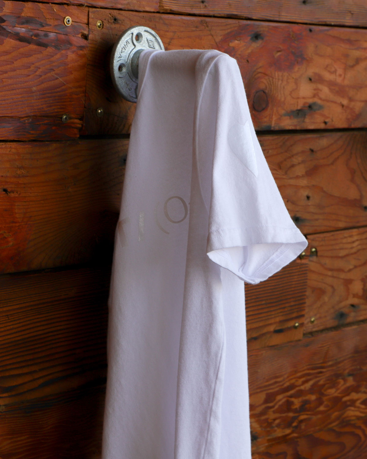 White Heart On logo t-shirt hanging on wood wall
