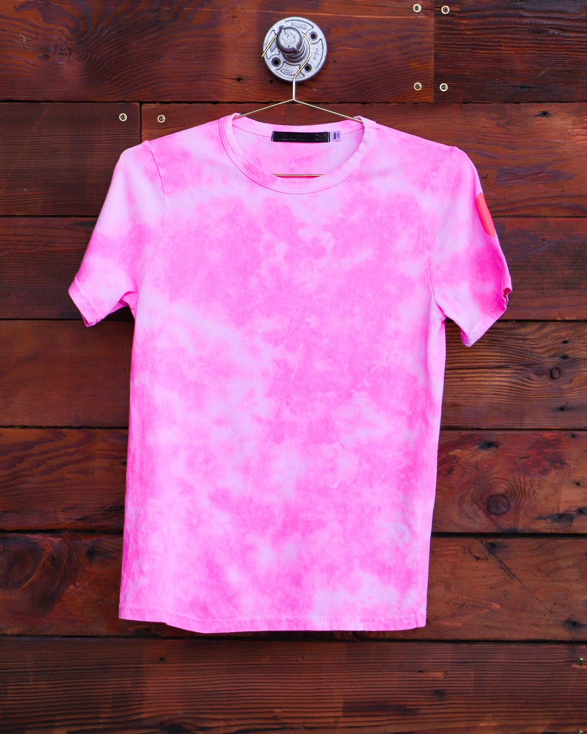 Pink hand-dyed tie dye t-shirt hanging on wood wall