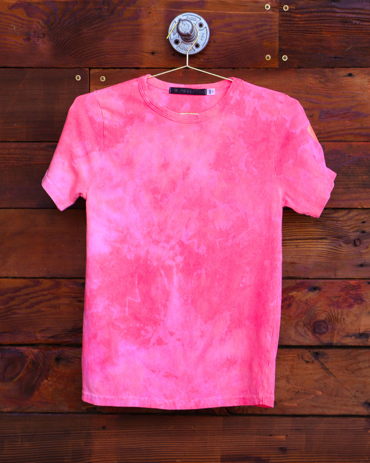 Bright salmon hand dyed tie dye shirt hanging on wood wall