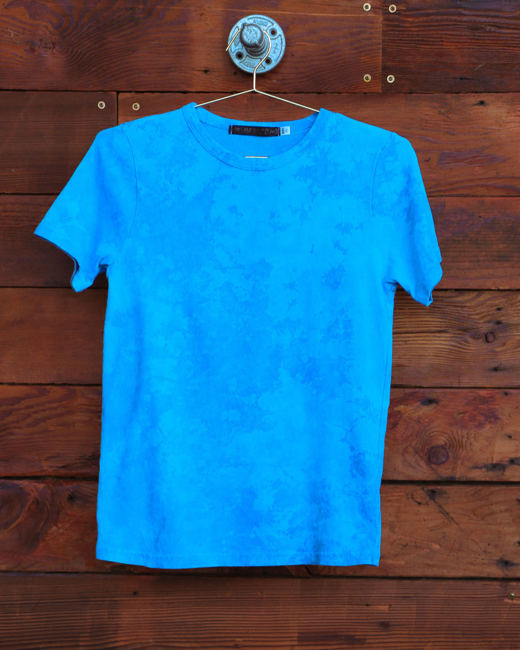 Blue hand dyed cloud tie dye t-shirt on a hanger in front of a weathered wood wall